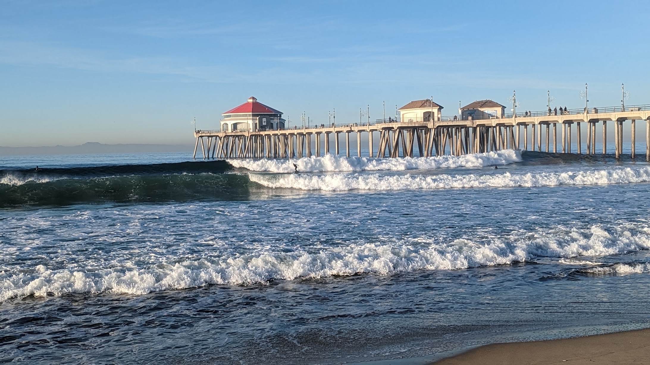 South side of the Huntington Beach pier with surfers in the water.